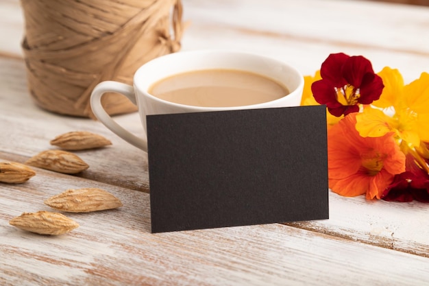 Maquete de cartão de visita de papel preto com flor de capuchinha laranja e xícara de café no espaço de cópia de vista lateral de fundo branco de madeira
