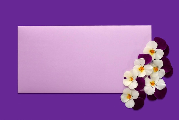 Foto maquete de convite com envelope lilás em branco sobre fundo roxo com flores de amor-perfeito