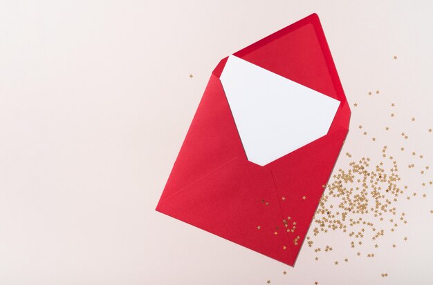 Maquete de envelope de papel quadrado em branco com confetes de estrelas vermelhas e douradas sobre fundo bege