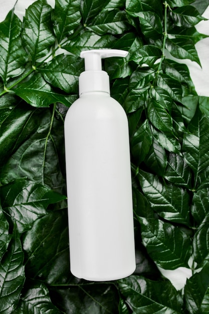 Maquete de garrafa branca em branco sobre folhas tropicais verdes, embalagem de cosméticos, vista superior do tubo de creme, composição plana leiga