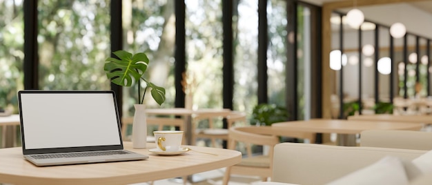 Maquete de laptop uma xícara de café e vaso de flores na mesa de madeira em uma cafeteria bonita e aconchegante