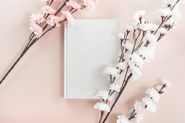 Maquete de livro branco aberto em um fundo rosa pastel com flor de cerejeira branca e rosa.