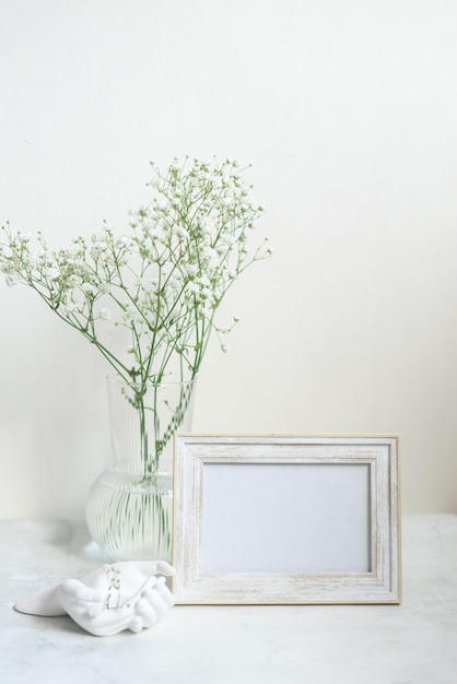 Maquete de moldura branca de retrato na mesa de madeira Vaso cerâmico moderno com gypsophila