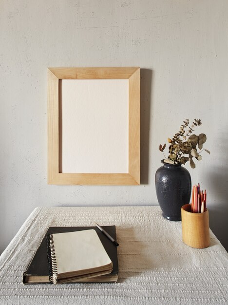 Maquete de moldura de madeira. design minimalista escandinavo. vaso de flores em uma pilha de livros sobre uma velha mesa de madeira. composição em uma superfície de parede branca