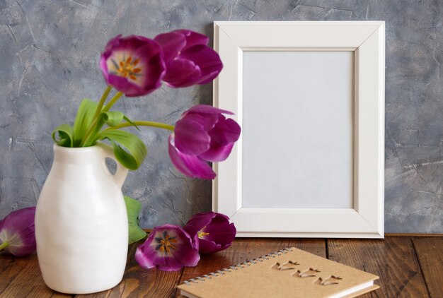 Maquete de moldura de pôster branco com tulipas roxas em um vaso perto da parede cinza