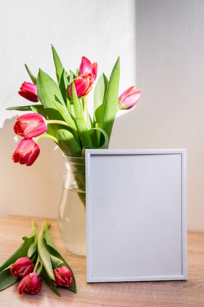 Maquete de moldura de retrato branco na mesa de madeira vaso moderno com tulipasinterior escandinavo