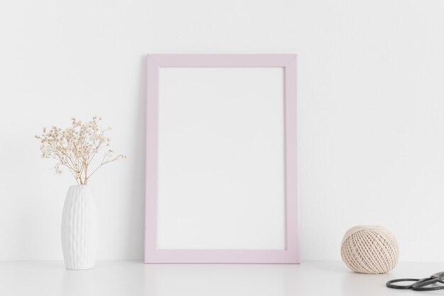 Maquete de moldura rosa com acessórios de espaço de trabalho e gypshophila em um vaso em uma mesa brancaOrientação de retrato
