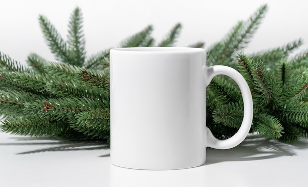 Maquete de Natal uma caneca de chá vazia branca sobre uma mesa branca e galhos de uma grinalda de árvore de Natal.