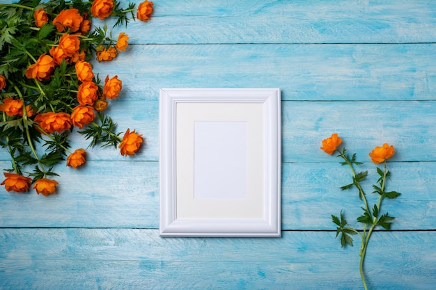 Maquete de quadro pequeno branco com buquê de flores na mesa de madeira azul. Moldura vazia simulada para arte de apresentação. Moldura de modelo para arte moderna.