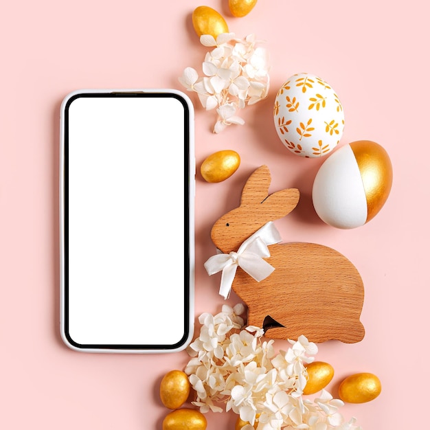 Foto maquete de smartphone com doces de ovos dourados de páscoa e flores em fundo rosa pastel conceito de férias feliz páscoa