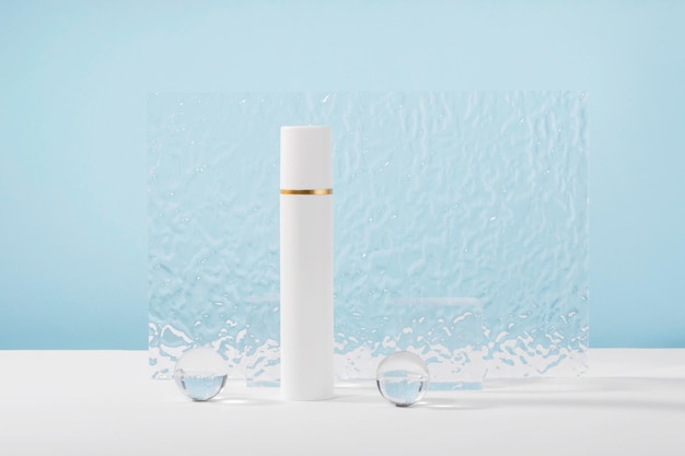 Maquete de tubo de plástico de creme cosmético sem marca em fundo azul com adereços elegantes bolas de vidro e placa de acrílico Corretivo de loção ou embalagem de produto de beleza branca Apresentação do produto