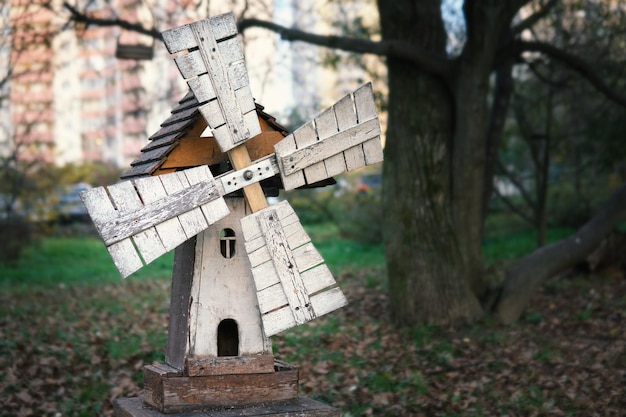 Maquete de um moinho de vento medieval de madeira em um parquinho infantil  com uma casa ao fundo