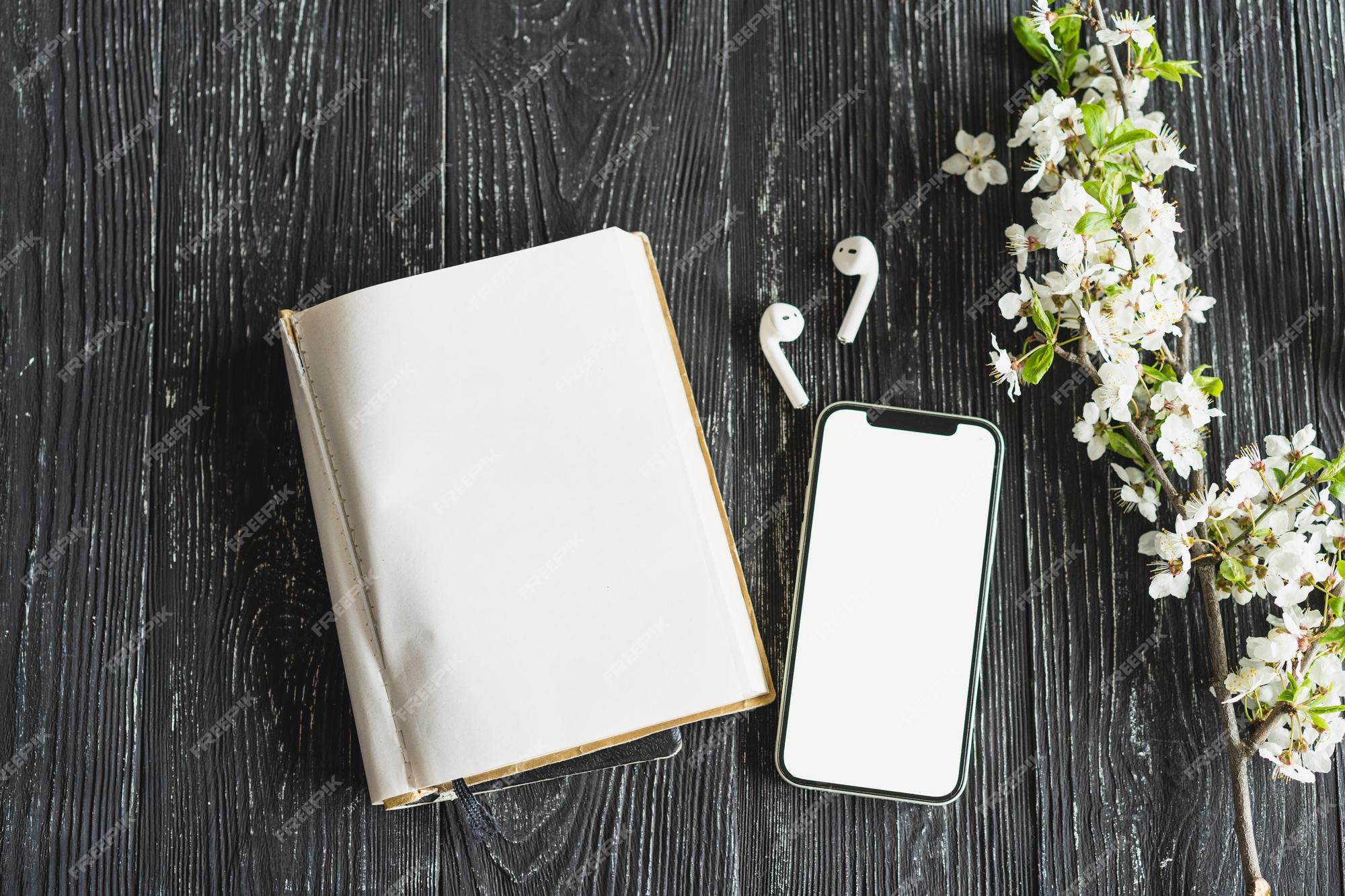 Maquete de telefone celular colocado horizontalmente com tela branca em  branco e fones de ouvido sem fio no fundo de uma velha mesa de madeira  vídeo do jogo aplicativos de áudio podcasts