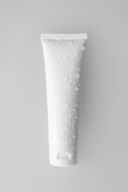 Maquete do tubo de plástico branco com creme hidratante, xampu ou limpador facial com gotas de água no fundo branco.