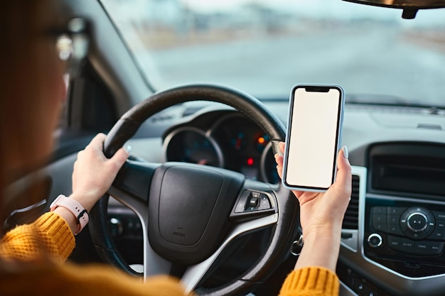 Maquete em branco da tela do telefone celular nas mãos de uma mulher motorista em um carro