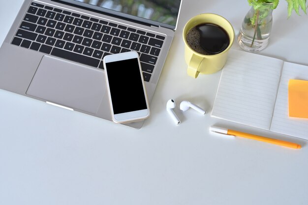 Maquete smartphone, laptop, fone de ouvido na mesa de escritório com uma xícara de café.