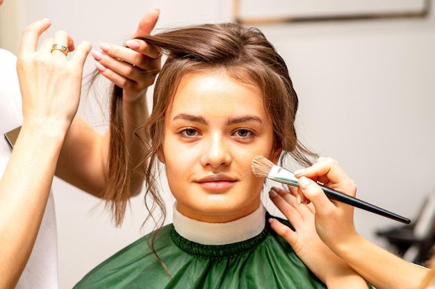 Maquiador e cabeleireiro preparam a noiva fazendo penteado e maquiagem em um salão de beleza