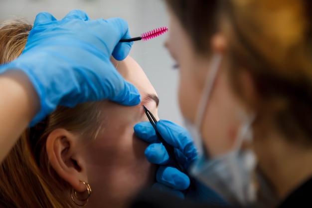 Maquiador faz correção de sobrancelha linda jovem bonita no salão de beleza. Atendimento ao cliente em salão de beleza para criar uma imagem incrível. Assistente de criação de maquiagem de trabalho. Satisfação com a beleza do conceito