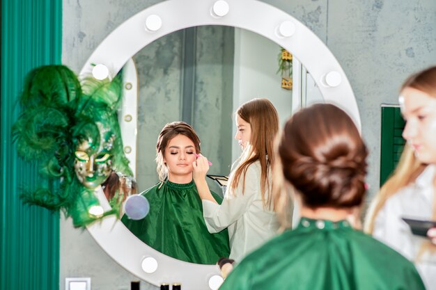 Maquiador fazendo maquiagem profissional para jovem em salão de beleza.