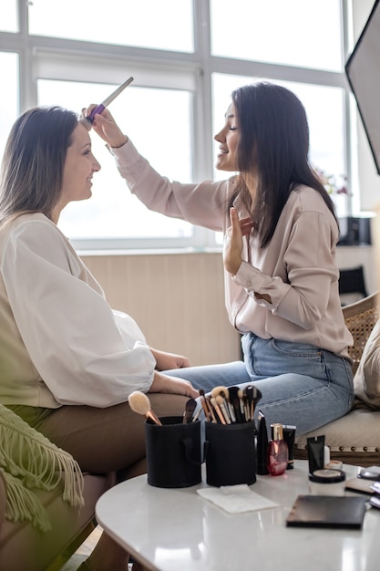 Maquiador feminino profissional aplicando cosméticos no rosto de modelo usando escova trabalhando no salão de beleza