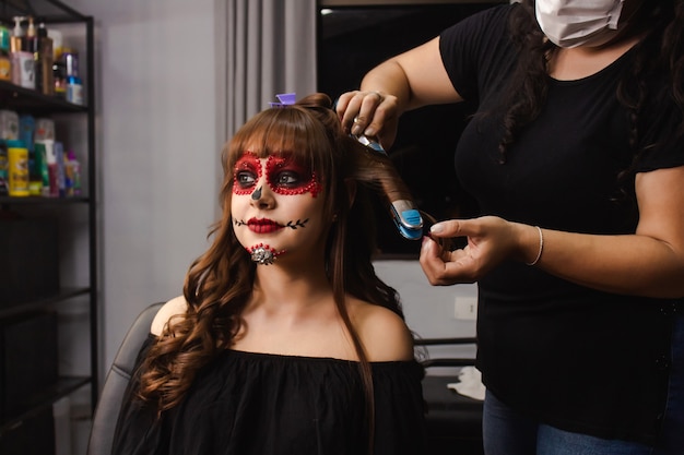 Maquiador ondulando o cabelo de uma menina com maquiagem Dia de los Muertos.