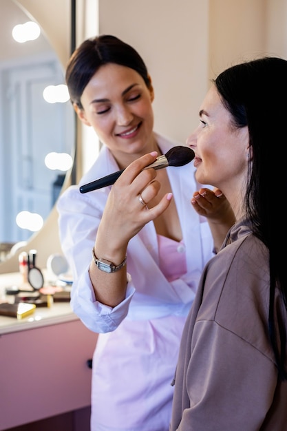 Maquiador profissional feliz aplicando lápis labial de cosméticos em cliente mulher trabalhando no salão de beleza