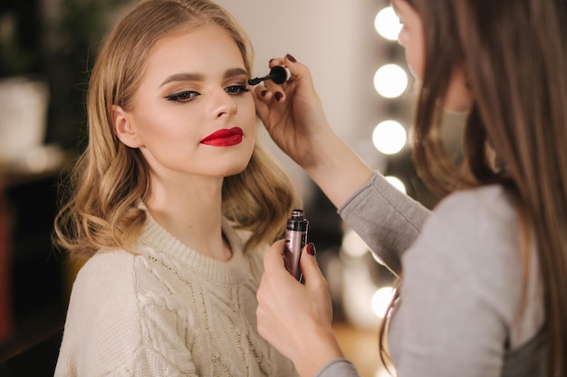 Maquiador trabalha no estúdio de beleza Mulher aplicando-se por mestre de maquiagem profissional Linda maquiadora faz uma maquiagem para modelo de cabelo loiro