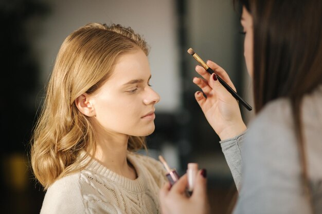 Maquiadora trabalha em seu estúdio de beleza Retrato de mulher aplicando-se por mestre de maquiagem profissional Linda maquiadora começa a fazer uma maquiagem para modelo de cabelo loiro