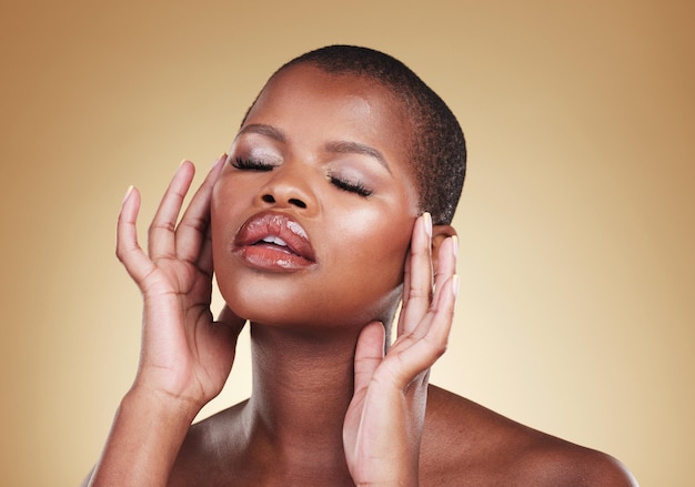 Maquiagem de beleza e uma mulher negra com as mãos no rosto em estúdio para brilho de cuidados com a pele e cosméticos Tiro na cabeça de pessoa africana ou modelo com dermatologia de brilho facial e bem-estar em um fundo bege