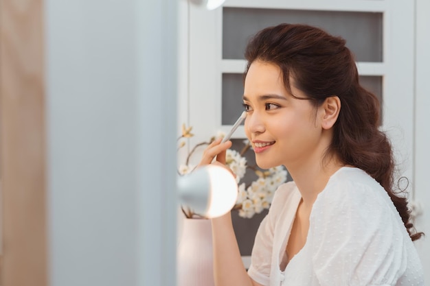 Maquiagem de beleza Mulher aplicando cosméticos na pele dos olhos com pincel na frente do espelho