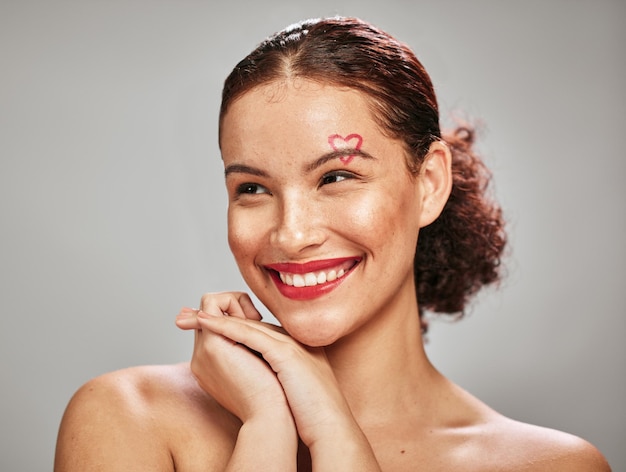 Foto maquiagem de mulher de beleza e rosto de coração de um modelo feliz em estúdio para cosméticos e dermatologia tiro na cabeça de pessoa estética com batom de cor vermelha para amor e ideia de cuidado facial do dia dos namorados