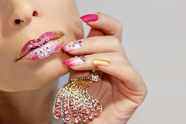 Maquiagem labial rosa e branca e manicure com strass