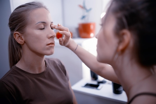 Maquiagem profissional no salão de beleza / mestre faz uma maquiagem profissional de verão fresca de uma bela modelo no salão