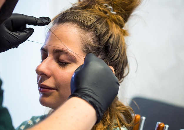 Maquillador depilarse las cejas con un hilo Cuidado facial profesional.