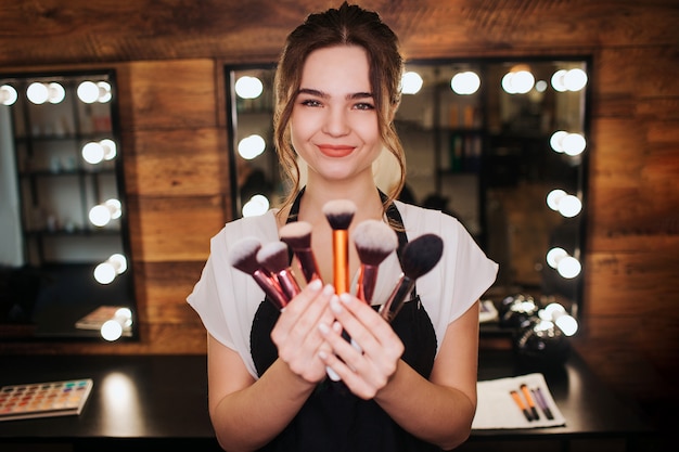 Foto maquillador joven sostenga un conjunto de pinceles en las manos