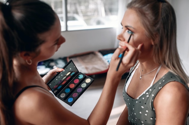 Foto el maquillador está maquillando a una joven hermosa con ojos grandes y hermosos, maquillaje colorido, moda