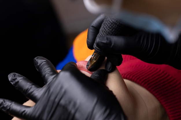 El maquillador permanente con guantes estériles negros se inclinó sobre la modelo y realiza el procedimiento de tatuaje de labios