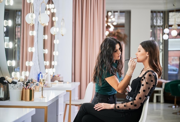 Un maquillador sonriente haciendo maquillaje para una mujer en un salón de belleza