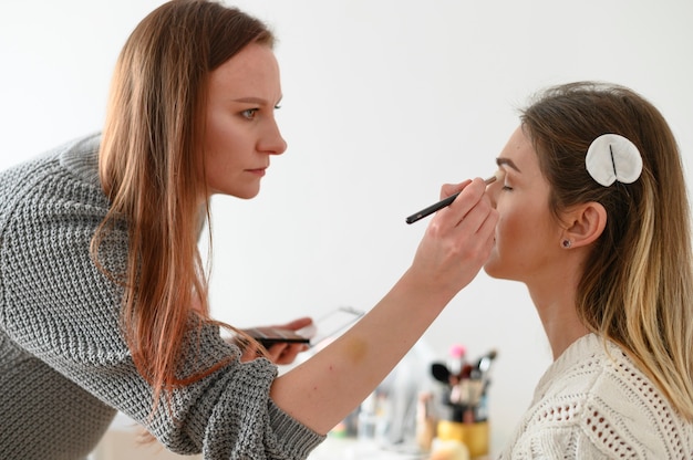 Maquilladora aplicando maquillaje de boda ligero en la cara de la mujer con paleta y pincel de maquillaje y belleza