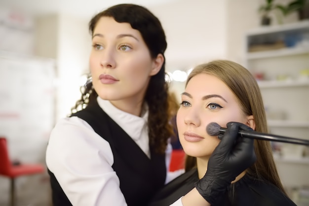 Maquilladora aplicando el tono de la base usando un pincel especial en la cara joven y bella modelo.