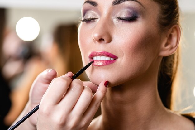 Maquilladora haciendo maquillaje profesional de hermosa mujer joven.