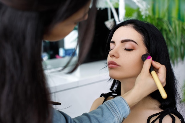 Maquilladora haciendo maquillaje profesional de modelo de mujer joven