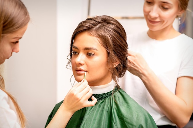 Maquilladora y peluquera preparan a la novia haciendo peinado y maquillaje en un salón de belleza