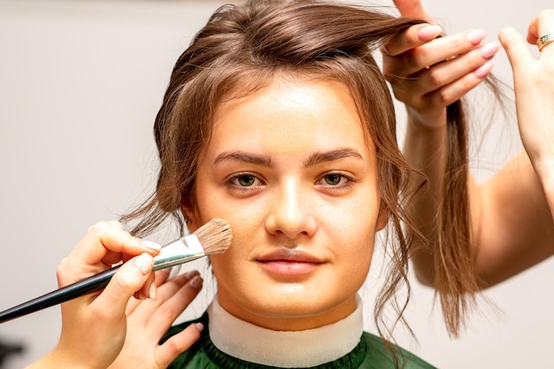 Maquilladora y peluquera preparan a la novia haciendo peinado y maquillaje en un salón de belleza