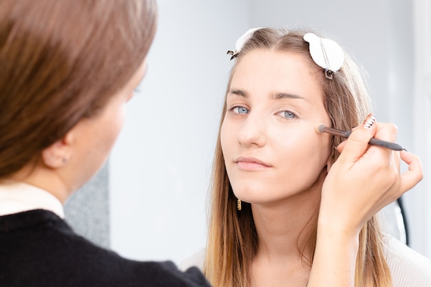 Foto maquilladora profesional aplica maquillaje a una hermosa modelo de niña. el rostro de una hermosa niña de piel limpia. concepto de maquillaje y cosmetología de la vida real