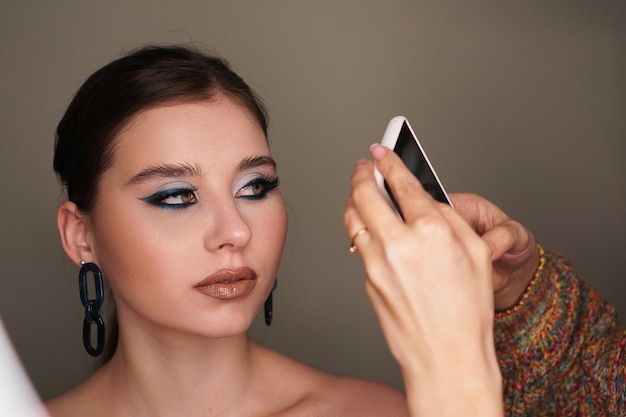 Maquilladora tomando foto móvil para el modelo con maquillaje de moda azul