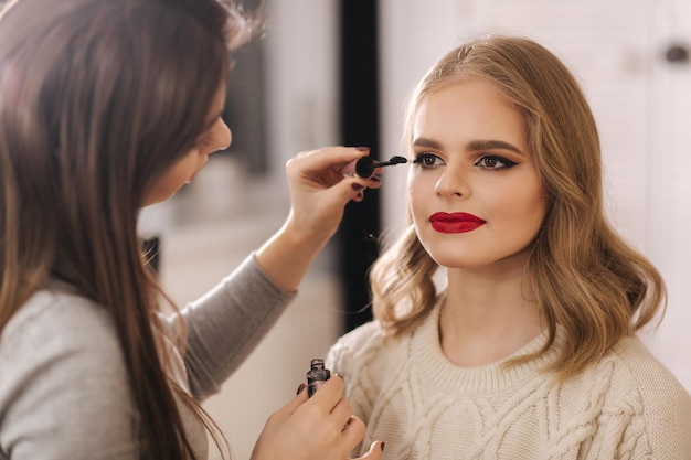 Maquilladora trabaja en estudio de belleza Mujer aplicando por maestro de maquillaje profesional Hermosa maquilladora hace un maquillaje para modelo de cabello rubio