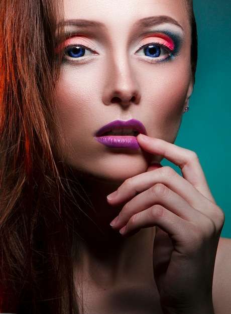 Maquillaje de arte de belleza en la cara de una chica mujer con pelo rojo. Chica perfecta con grandes ojos azules sobre un fondo verde. Cosmética profesional para el cuidado de la piel del rostro y el cuerpo.