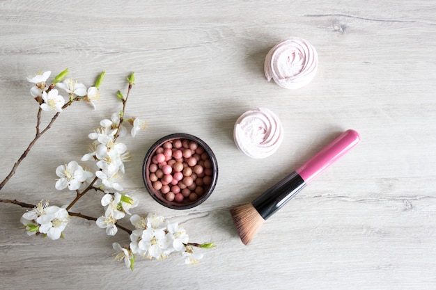 Maquillaje Balls rubor cosmética natural para el cuidado de la piel. Ramita de cerezo en flor en una mesa de madera. Concepto de cosmetología y spa