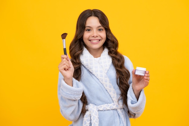 Maquillaje de belleza y cosméticos para niños Adolescente con pincel aplicando rubor en la cara aislado sobre fondo amarillo de estudio